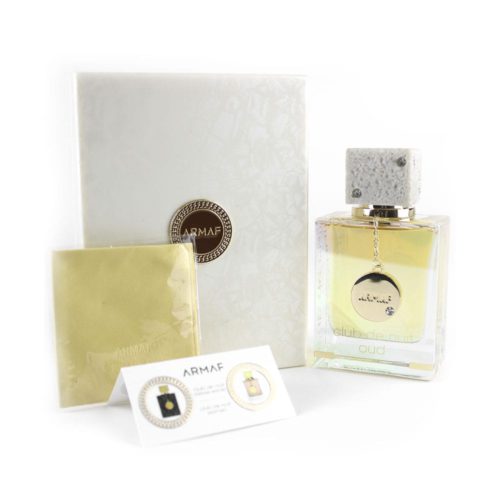 Club de Nuit Oud eau de parfum de Armaf, que presenta un frasco rectangular transparente con un tapón blanco jaspeado adornado con pequeños cristales. El frasco incluye un medallón dorado colgante y se presenta junto a una caja blanca con acabado texturizado y el logotipo de Armaf. También se muestra una pequeña tarjeta informativa.