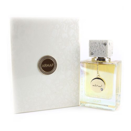 Club de Nuit Oud eau de parfum de Armaf, que se presenta en un frasco rectangular transparente con un tapón blanco jaspeado adornado con pequeños cristales y un colgante de medallón dorado. La botella se muestra junto a una caja texturizada blanca con un medallón dorado con el logotipo de Armaf.