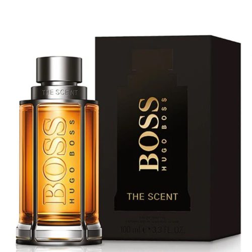 Boss The Scent Eau de Toilette 100 ml para hombre de Hugo Boss. La imagen muestra el frasco del perfume y su caja. El frasco tiene un líquido de color ámbar en su interior con un tapón y un marco metálicos, y la palabra 'BOSS' grabada en relieve verticalmente. La caja es negra con el texto "BOSS Hugo Boss The Scent" en letras doradas.