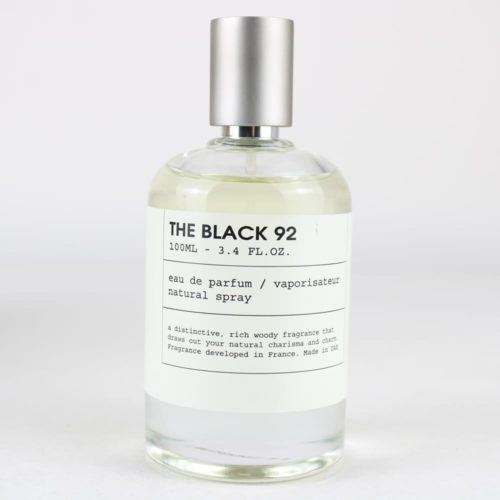 THE BLACK 92 Eau de Parfum de Milestone: frasco transparente minimalista con tapón plateado y etiqueta sencilla, que ofrece una rica fragancia amaderada, 100 ml.