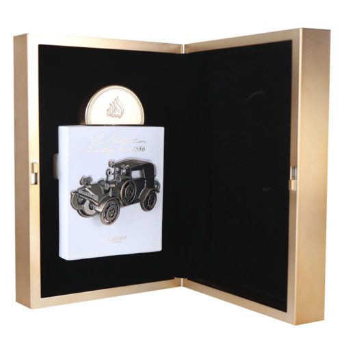 Vista de la caja abierta de La Collection D'antiquités 1886 Eau De Parfum de Lattafa, que revela un frasco blanco con un diseño de coche antiguo dentro de un estuche dorado.